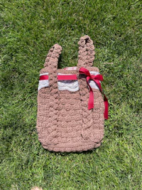 a brown crocheted tote bag laying on the grass