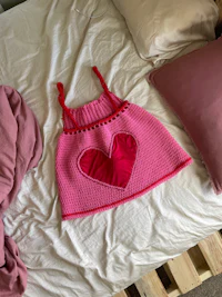 a pink crocheted dress on top of a bed