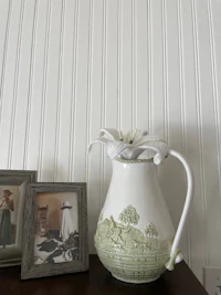 a white pitcher on a table next to a picture frame