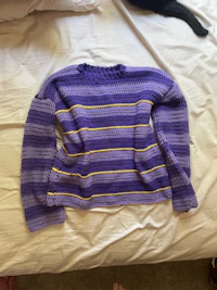 a purple and yellow sweater is laying on top of a bed
