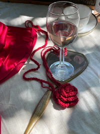 a glass of wine on a table next to a mirror and a crocheted rose