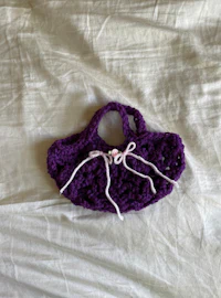 a purple crocheted bag on a white bed
