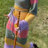 a woman in a colorful knitted dress holding a broom