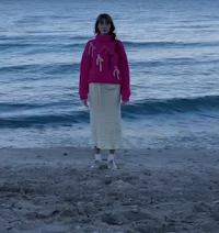 a woman standing on the beach wearing a pink jacket and skirt